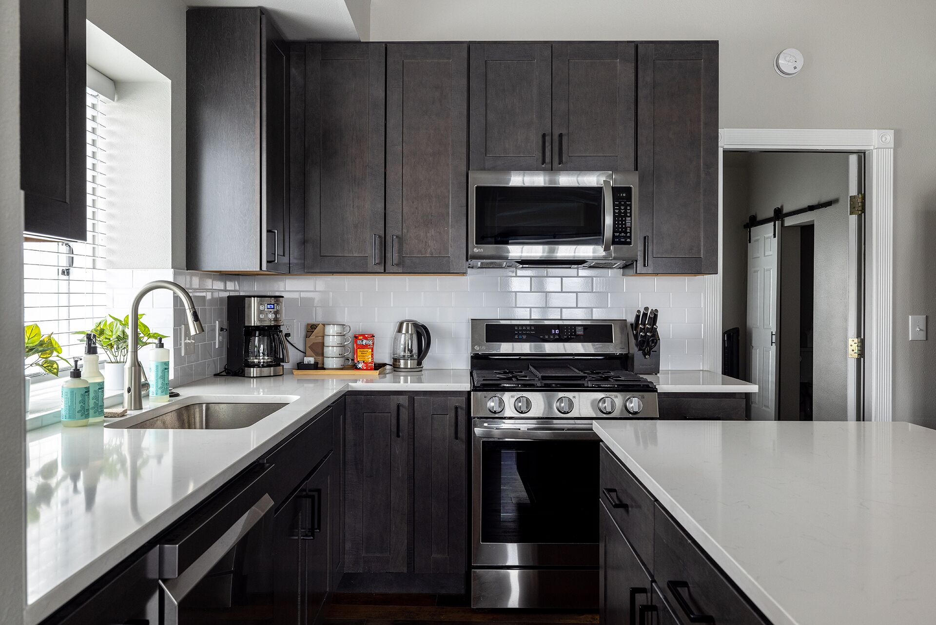 A modern kitchen with dark cabinets, stainless steel appliances, and a white countertop.