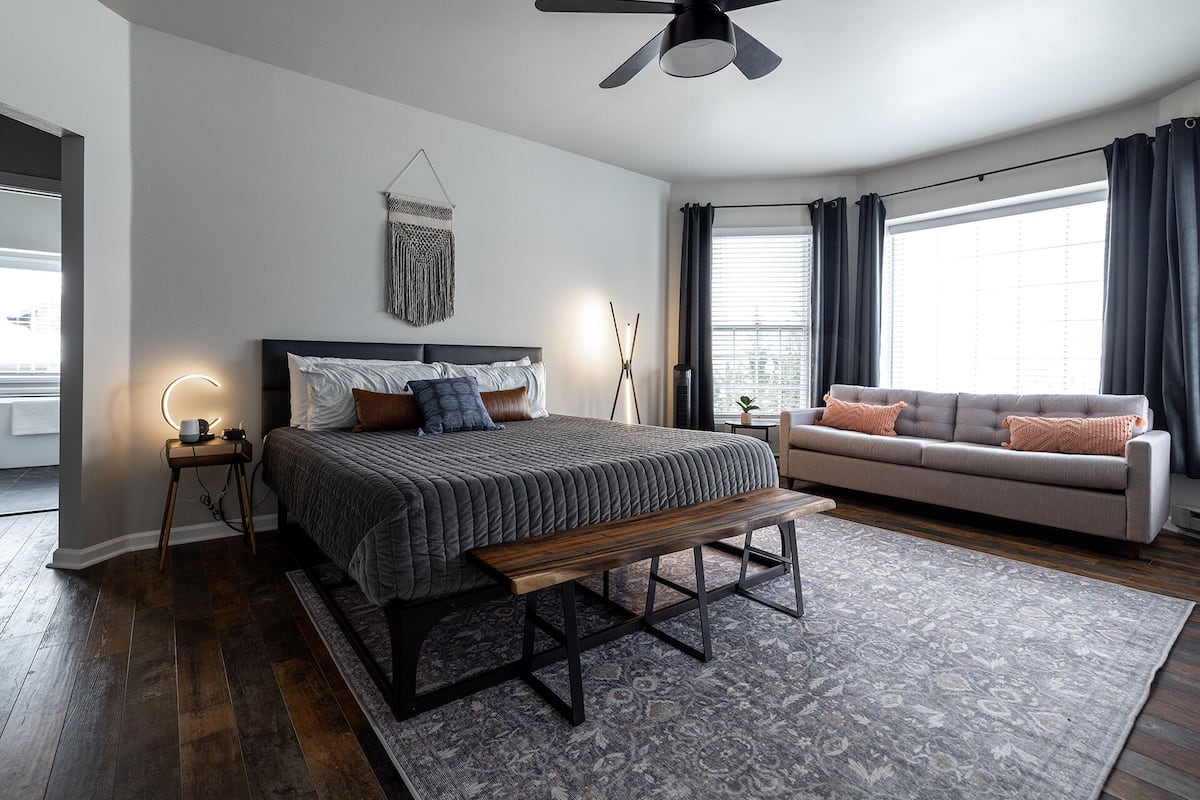 Ein modernes Schlafzimmer mit Bett, Sitzbank, Nachttisch und einer Couch.