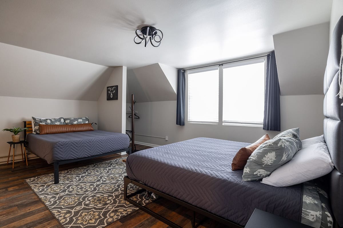 Ein Schlafzimmer mit zwei Betten, einem großen Fenster mit Vorhängen, einer Deckenleuchte und einem gemusterten Teppich.