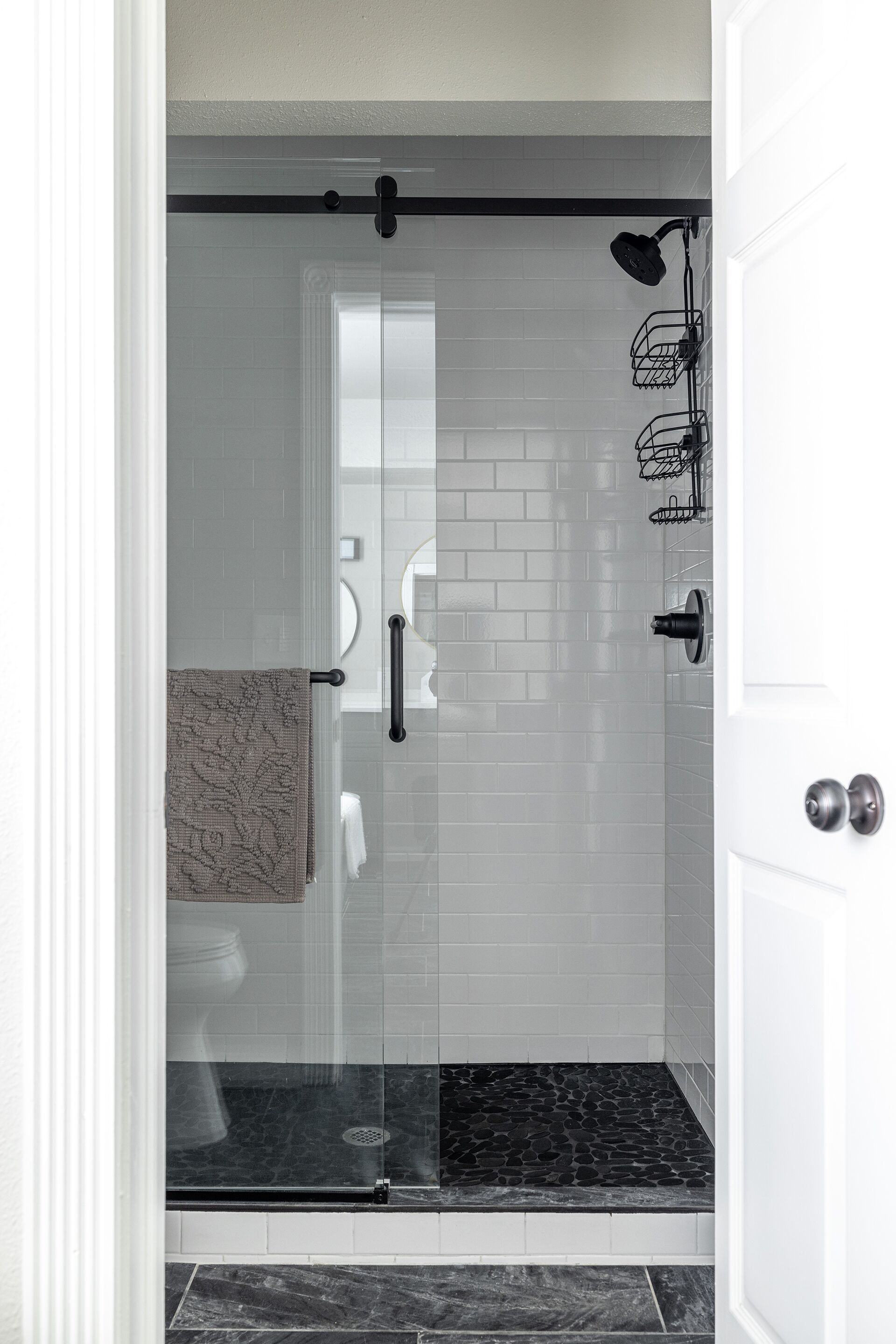 Un baño moderno con cabina de ducha de vidrio, paredes con azulejos blancos y suelo de mármol.