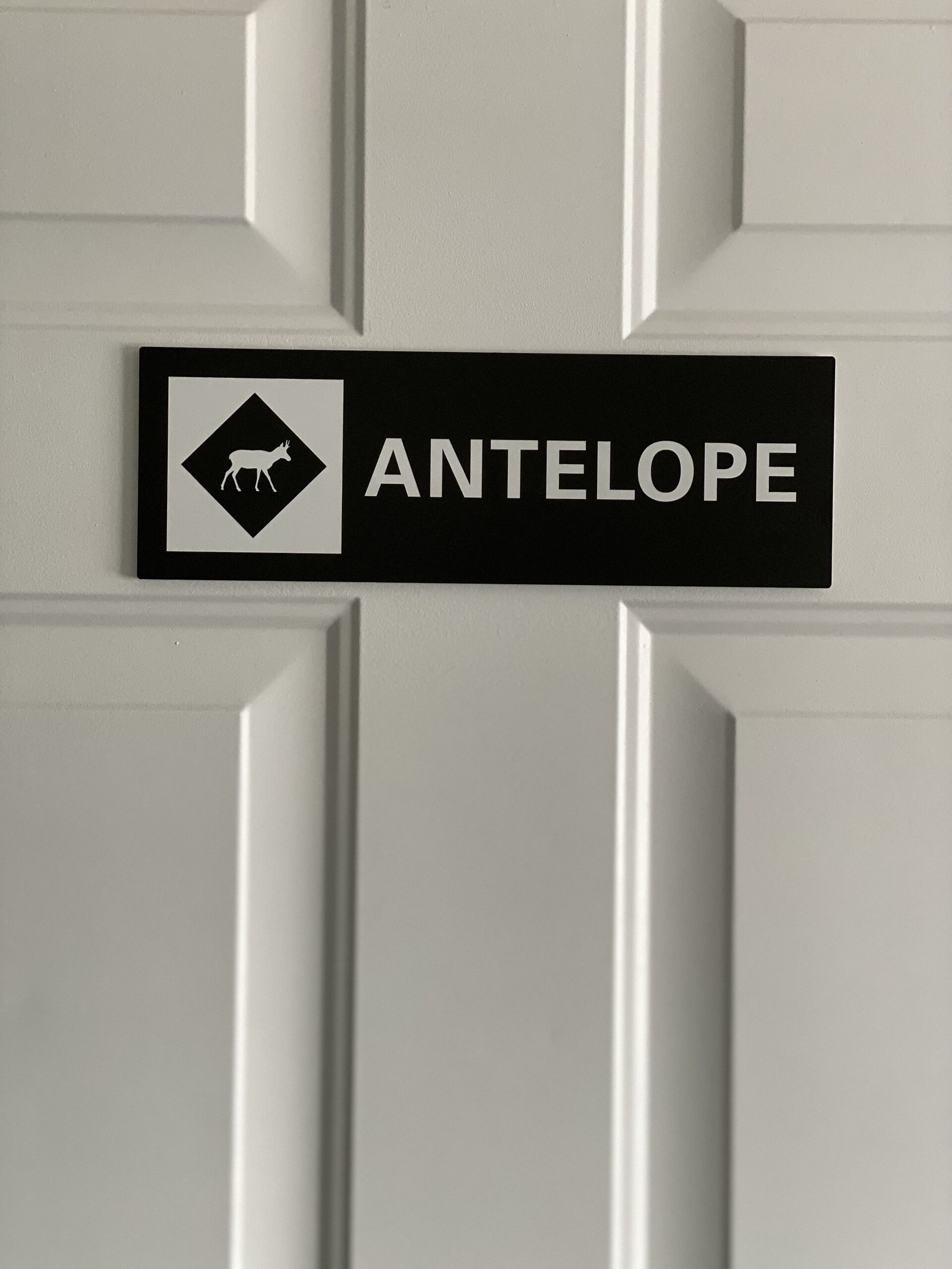 Une enseigne représentant un cerf et portant le mot « ANTILOPE », fixée sur une porte blanche.