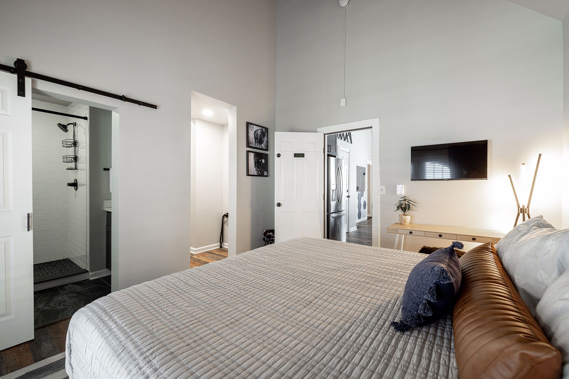 Un dormitorio con una cama, una mesita de noche, un televisor y una puerta que da a otra habitación.