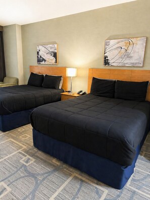 Een hotelkamer met twee bedden, een nachtkastje met een lamp en kunstwerken aan de muur.