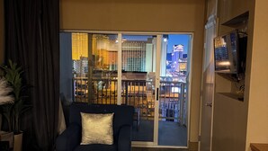 Un salon avec un canapé, un vase de roses rouges, un téléviseur et une vue sur le paysage urbain, visible à travers une porte vitrée.