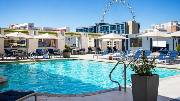 Un espace piscine avec des chaises longues, des parasols et une grande roue en arrière-plan.