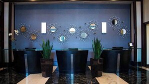 Un espace d’accueil avec un mur bleu, de nombreux miroirs et deux comptoirs de réception.
