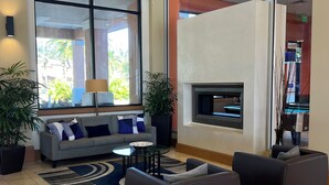 A spacious lobby with a grey sofa, two armchairs, a glass coffee table, and a fireplace.
