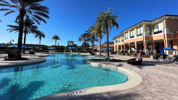 A swimming pool with a 4 ft. 0 in. depth marker, surrounded by palm trees and lounge chairs, with a building in the background.