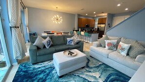 A modern living room with two sofas, a coffee table, and a patterned rug. There is a dining area with chairs and a table in the background.