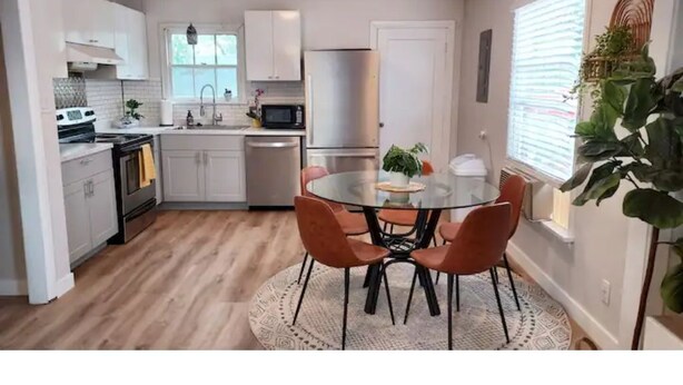 A modern kitchen with white cabinets, stainless steel appliances, and a round dining table with orange chairs.