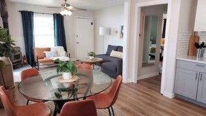 A modern living room with a glass dining table, two sofas, and a kitchen area with white cabinets.