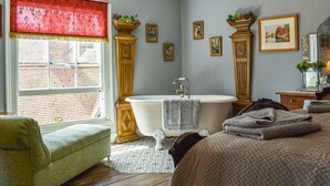 Een slaapkamer met een bed, een groene fauteuil, een ligbad op pootjes en een raam met een rode gordijntje.
