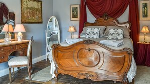 Een slaapkamer met een houten bed, rode gordijnen, een spiegel en een bureau met een stoel.