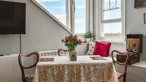 Een eetgedeelte met een tafel gedekt voor twee personen, een vaas met bloemen en een raam met uitzicht op de lucht.