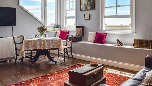 Een gezellige kamer met een eettafel, stoelen, een bank en een vensterbank.