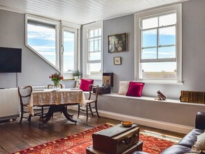 Een gezellige kamer met een eettafel, stoelen, een bank en een vensterbank.