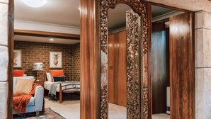 A bedroom with a brick wall, a bed with a patterned bedspread, and a large mirror with ornate woodwork.