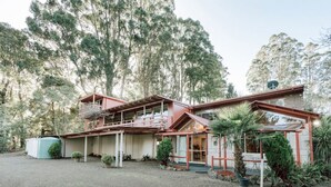 A two-story house with a balcony, surrounded by trees and a gravel driveway.