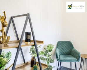 Ein modernes Interieur mit einem mit Grün gepolsterten Sessel, einem Holzregal mit Dekoration und dem Logo von Passion Fruit Properties.