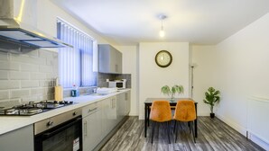 A modern kitchen with a gas stove, microwave, and a dining area with two chairs and a table. - 52NRC Unli Wi-fi 3 Bedroom House (Coventry)