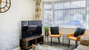 A living room with a flat-screen TV, two orange chairs, a small round table, and a window with blinds. - 52NRC Unli Wi-fi 3 Bedroom House (Coventry)