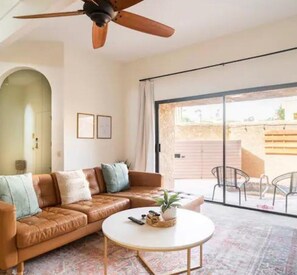 Ein Wohnzimmer mit braunem Ledersofa, einem runden Couchtisch und einem Deckenventilator.