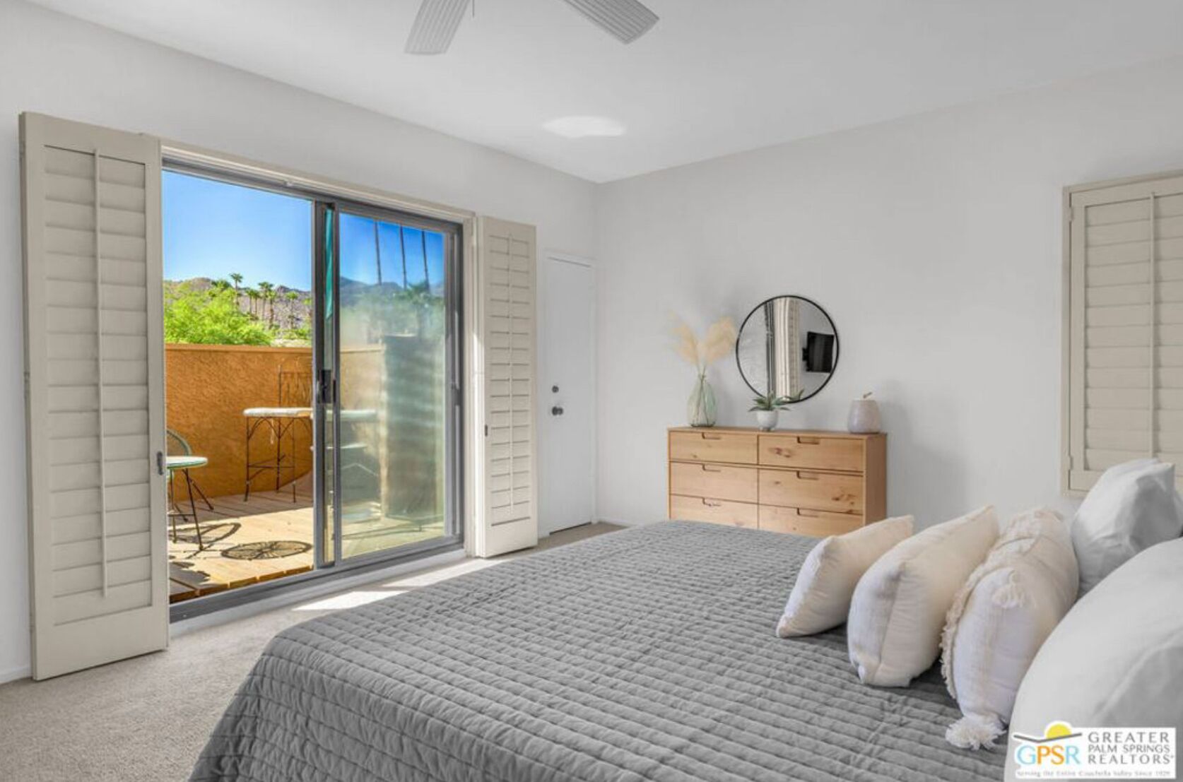 Een slaapkamer met een groot bed, een dressoir, een spiegel en een schuifdeur die leidt naar een terras met tuinmeubilair.