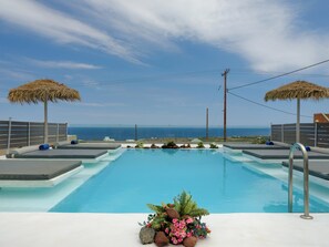 A swimming pool with a view of the ocean, surrounded by lounge areas and thatched umbrellas.