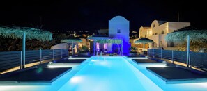 A pool area with a water feature and a building with a white facade and blue lighting in the background.
