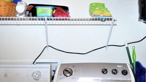 Een wasruimte met een voorlader wasmachine en droger, planken erboven met diverse spullen, en een stroomkabel langs de muur.