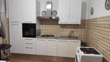 Une cuisine de taille réduite avec des meubles blancs, un four encastré, une cuisinière à gaz et un évier.