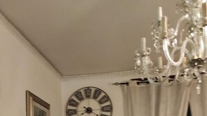 Un couloir avec un tapis à motifs, une horloge murale, un lustre et une porte donnant sur une autre pièce.