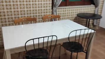 Une table à manger avec quatre chaises, une fenêtre avec des rideaux et un mur orné d’un motif.