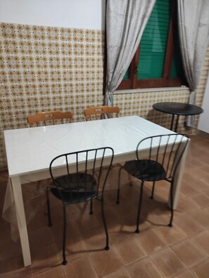A dining table with four chairs, a window with curtains, and a patterned wall. - Sunny Seaside Escape in San Pier Marina (San Pier Niceto)