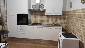 Une cuisine de taille réduite avec des meubles blancs, une cuisinière à gaz, un évier et un lave-linge.