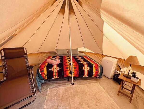 A cozy tent with a bed, a chair, and a small table with a lamp.