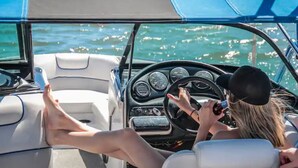 A boat interior with a steering wheel, dashboard, and a person holding a smartphone. - Cozy Bell Tent Retreat at Lake Texoma (Kingston)