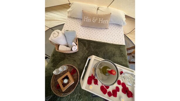 A neatly arranged bedroom with a bed, a bedside table with a tray of rose petals and a candle, and a decorative pillow with "His & Hers" on it. - Cozy Bell Tent Retreat at Lake Texoma (Kingston)