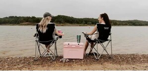 Two people sitting on folding chairs by a lake with a cooler and a water bottle between them. - Cozy Bell Tent Retreat at Lake Texoma (Kingston)