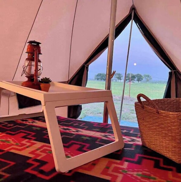 A tent interior with a table, a lantern, and a view of the outdoors.