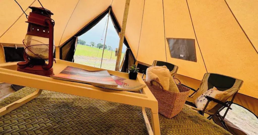 A tent interior with a table, a lantern, a basket, and a chair.