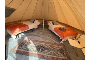 Two beds are arranged in a semi-circle, each with a pillow and blanket, and a small table with a chair nearby.