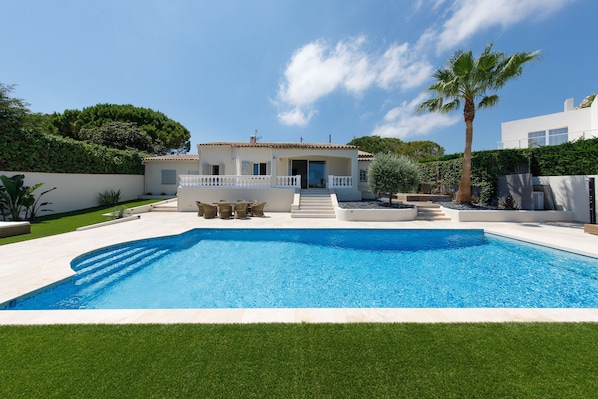 Une maison moderne dotée d’une piscine, d’un patio avec mobilier d’extérieur et d’une pelouse bien entretenue.