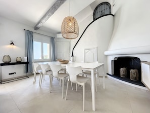 Un espace de salle à manger moderne avec une table et des chaises blanches, un luminaire suspendu et une cheminée.