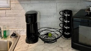 A kitchen with white cabinets, a marble countertop, a coffee maker, a fruit basket, and a microwave.