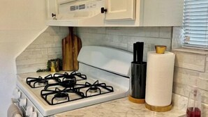 A kitchen with white cabinets, a gas stove, a stainless steel sink, and a marble countertop.