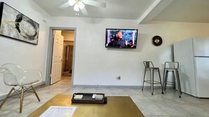 A living room with a TV, a coffee table with papers, a chair, and a refrigerator.