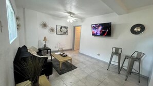 A living room with a sofa, coffee table, TV, and two bar stools.