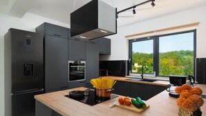 A modern kitchen with a large island, built-in appliances, and a view of greenery outside.