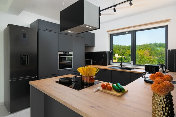 A modern kitchen with a large island, built-in appliances, and a view of greenery outside.